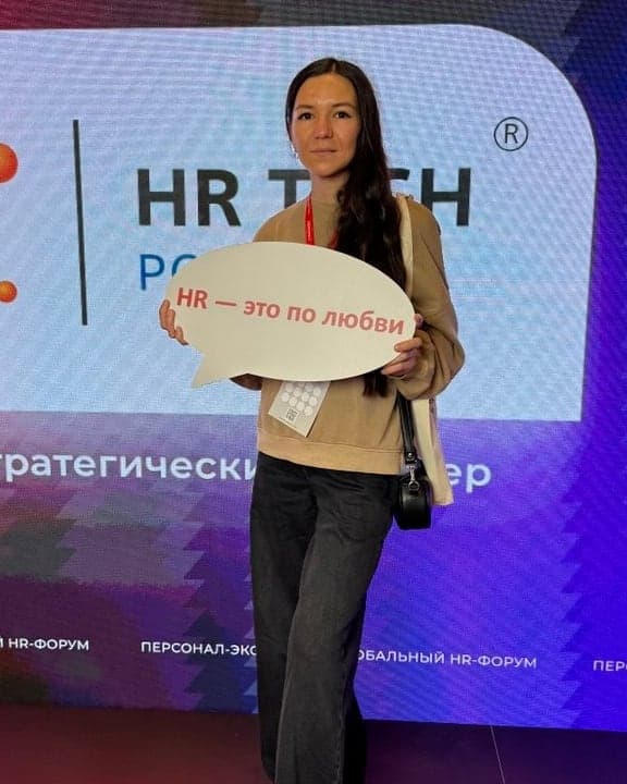 Анастасия в зоне HR TECH форума «Персонал Экспо» 2026 с табличкой «HR — это по любви»